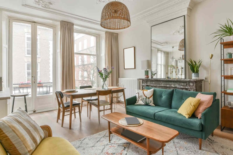 An oversized mirror hanging over a green velvet sofa illustrating-the-proper width difference between the two.